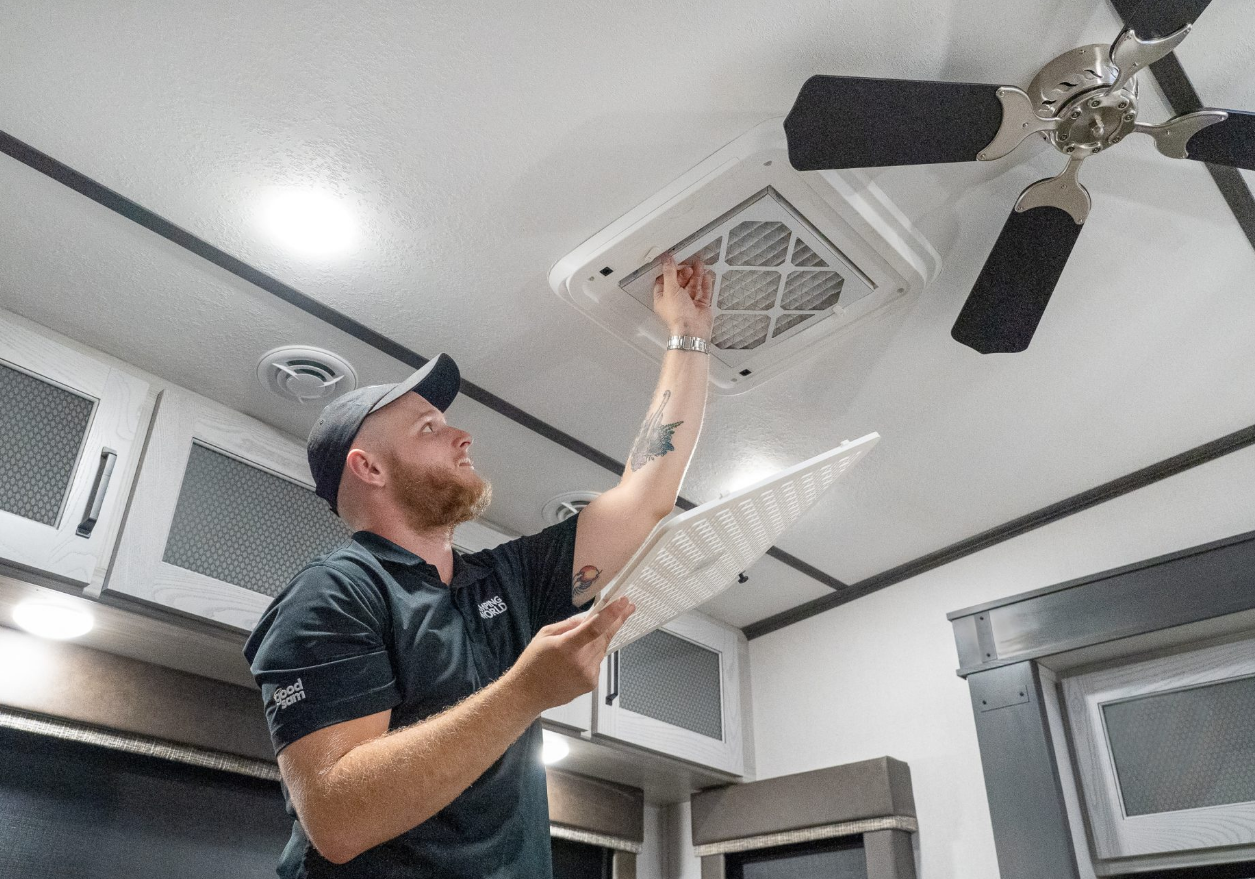 Technician inspecting RV AC capacitor inside rooftop unit